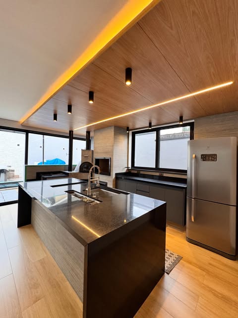 Cozinha ampla com ilha central em pedra escura, executada pela Aquarela Mármores